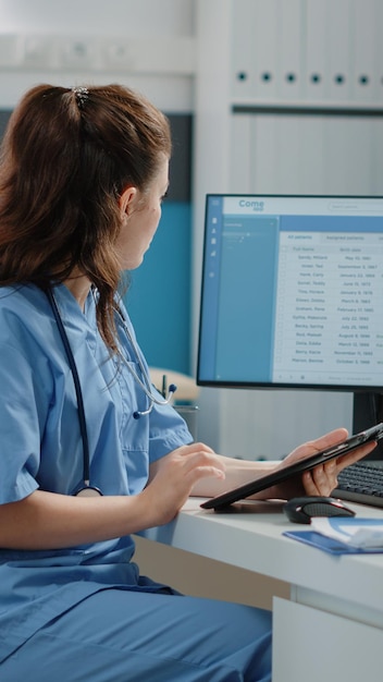 Assistente médico trabalhando com computador e tablet digital para sistema de saúde e consultas. enfermeira de mulher segurando o dispositivo com tela de toque no consultório do médico para visita de check-up anual.