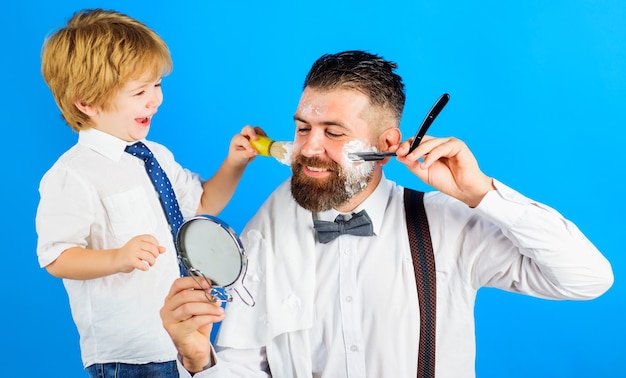 Assistente para o pai. filho e pai raspando a barba juntos. barbearia. cuidado com a barba. pequeno barbeiro.