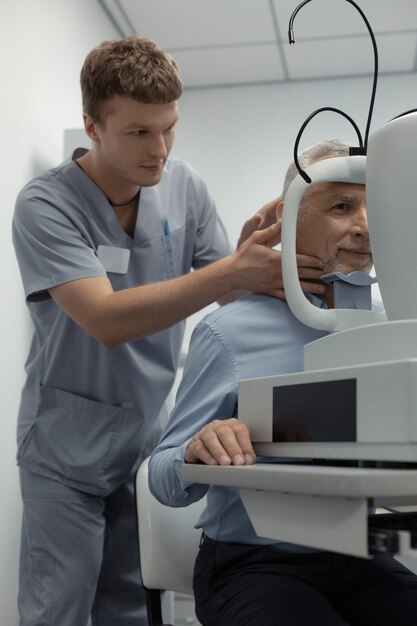 Assistente próximo ao paciente. Assistente oftalmologista de cabelos escuros vestindo uniforme em pé perto do paciente