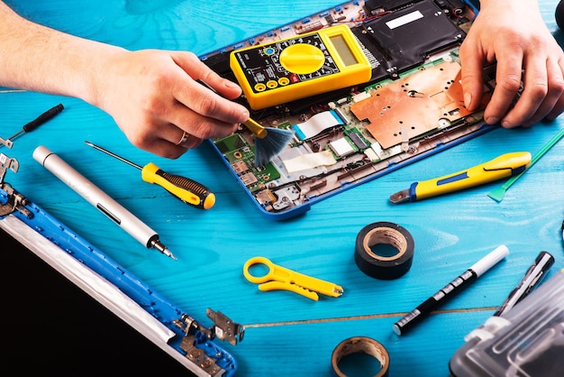 Assistente repara laptop com ferramentas e mãos na vista superior da mesa de madeira azul