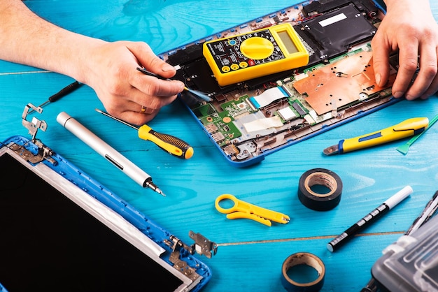 Assistente repara laptop com ferramentas e mãos na vista superior da mesa de madeira azul
