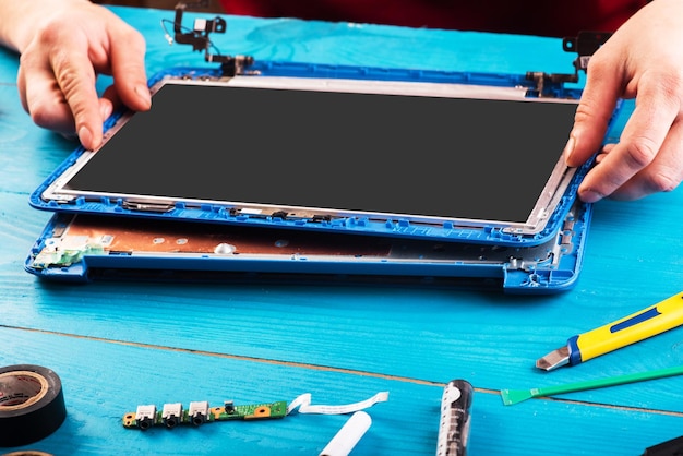 Foto assistente repara laptop com ferramentas e mãos na vista superior da mesa de madeira azul