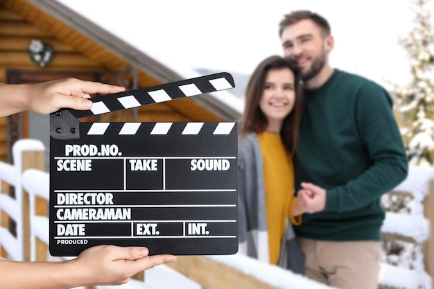 Assistente segurando claquete e jovem casal ao ar livre em um dia de neve closeup Produção de cinema