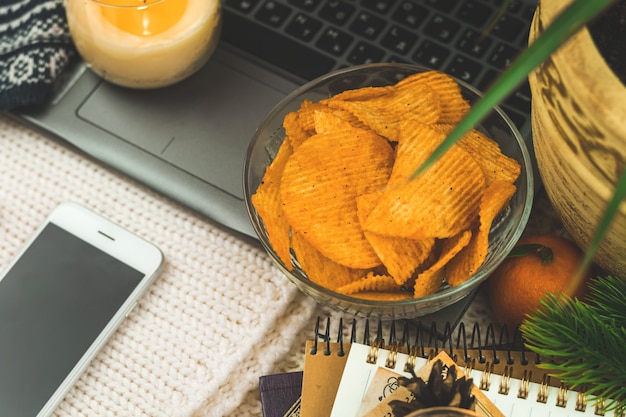 Assistindo filme em casa sozinho, alimentos pouco saudáveis, lanche, batata frita na tigela, laptop, fundo aconchegante de inverno. foto de alta qualidade