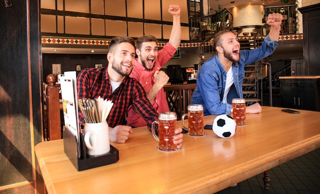 Foto assistindo futebol no bar. amigos felizes bebendo cerveja e torcendo pelo time favorito, comemorando a vitória.