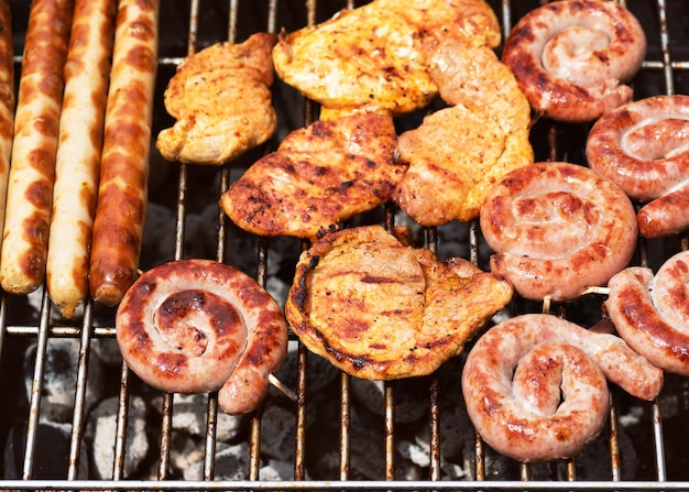 Assorted deliciosas carnes grelhadas sobre o fogo quente em um churrasco portátil com bifes salsichas