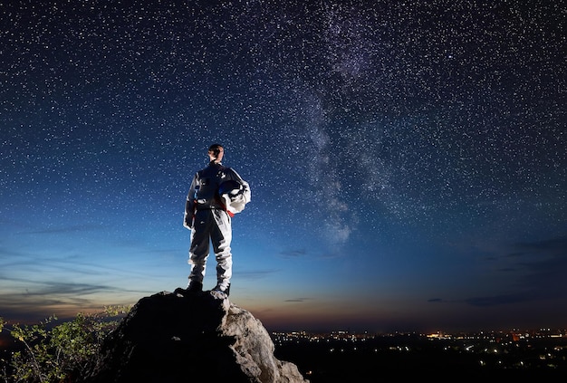 Astronaut, der auf felsigem Berg unter nächtlichem Sternenhimmel steht