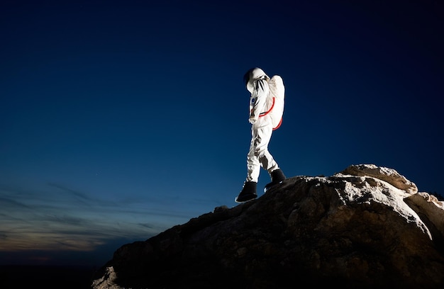 Astronaut, der den felsigen Berg unter dem Nachthimmel hinuntergeht