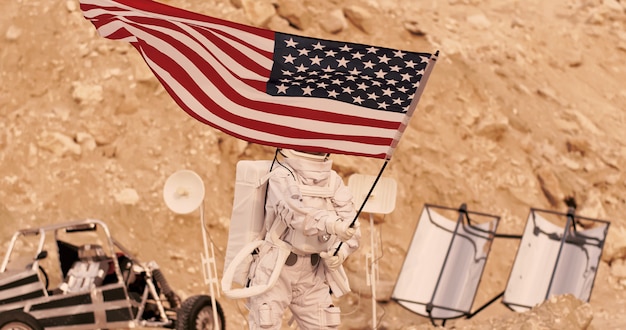 Astronaut mit der amerikanischen flagge, die auf rocky mountain des ausländischen roten planeten / des mars steht. erste bemannte mission auf dem mars