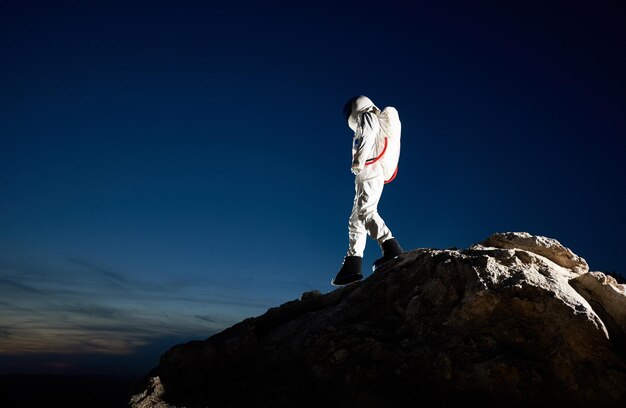 Astronauta caminando por la montaña rocosa bajo el cielo nocturno