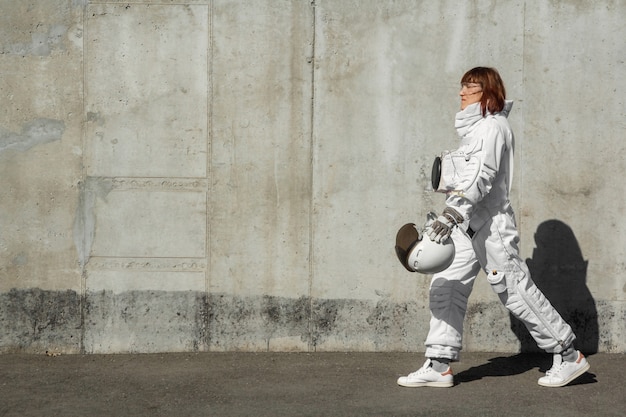 Astronauta hermosa chica sin casco en el fondo de una pared gris. Traje espacial fantástico.