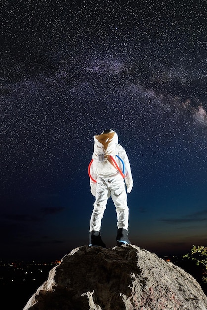 Astronauta parado en una montaña rocosa bajo un cielo estrellado.