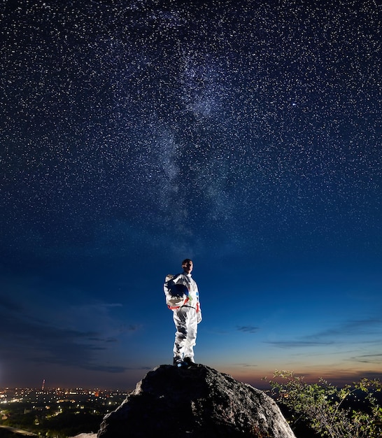 Foto astronauta de pie en la montaña rocosa bajo el cielo estrellado de la noche