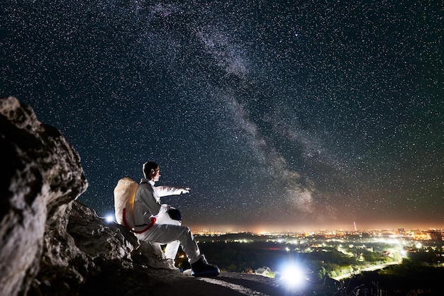 Astronauta sentado en una colina rocosa bajo un hermoso cielo nocturno con estrellas