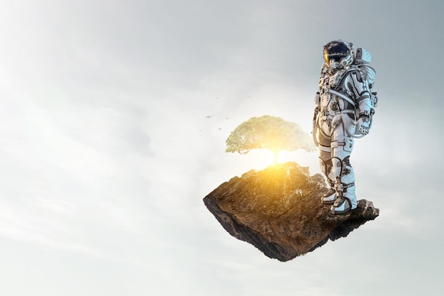 Astronauta sobre fondo de cielo nublado y árbol verde. Técnica mixta