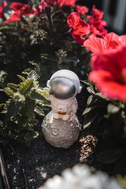 Astronautenfigur steht zwischen roten Blumen