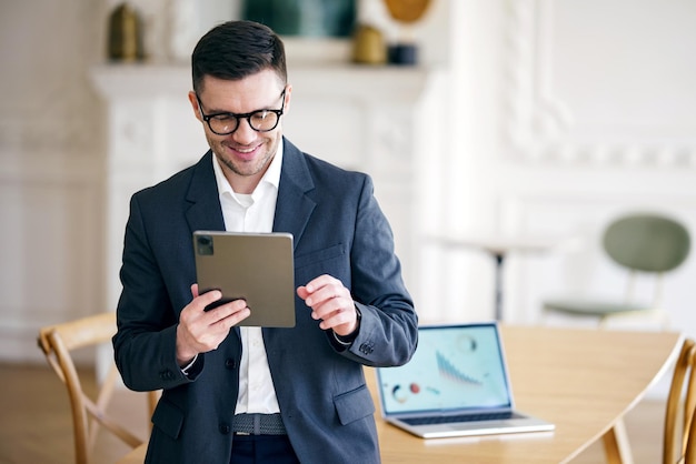 Foto un astuto hombre de negocios analiza datos en su tableta de pie en una habitación bien equipada