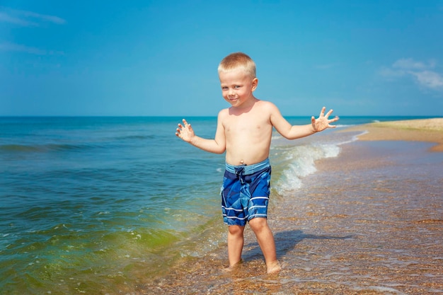 Astuto y sonriente niño encantador con pantalones cortos azules en el mar en un día soleado Turismo recreativo activo y viajes