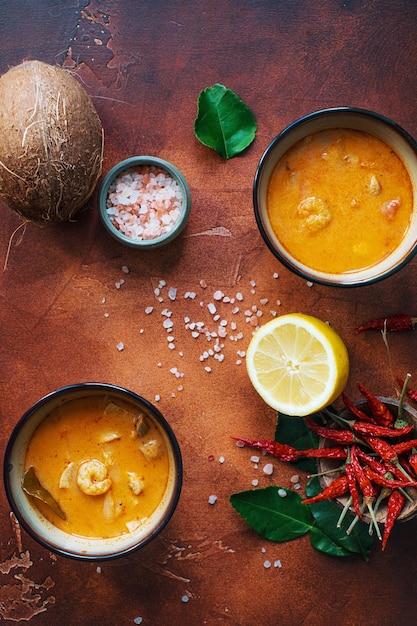 Asty asiatische Suppe Tom Yam in kleinen Schüsseln Chilipfeffersalz und Kokosnuss und Limette auf dunkelbraunem Hintergrund