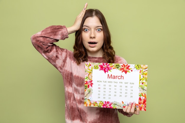 Asustada poniendo la mano en la cabeza hermosa joven en el día de la mujer feliz celebración de calendario