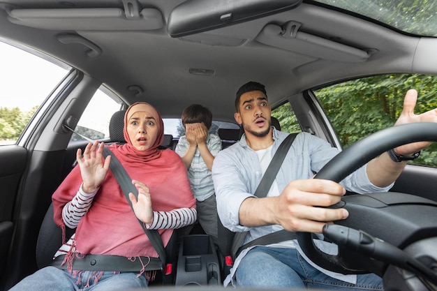 Foto asustado, conmocionado, esposo musulmán, esposa en hiyab y niño con los ojos cerrados en la cabina del automóvil durante el incidente