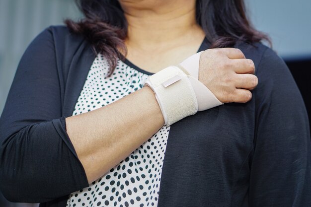 Atadura elástica do uso asiático da senhora em sua mão no escritório.