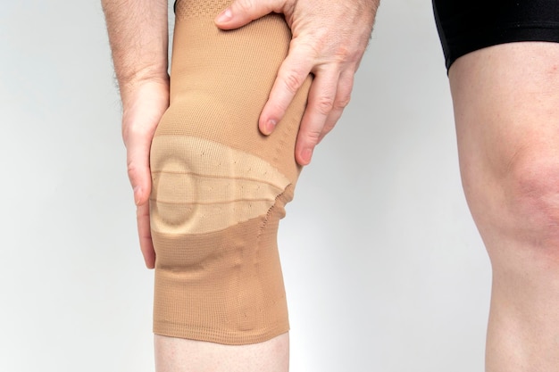 Atadura para fixar o joelho lesionado da perna humana em fundo branco. medicina e esportes. tratamento de lesão de membro