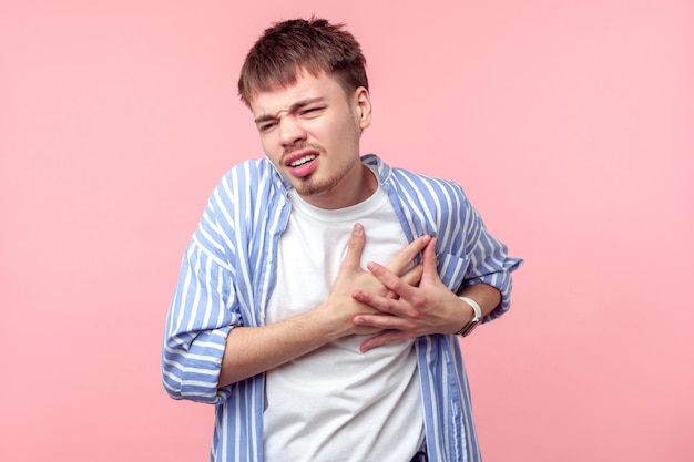 Ataque cardíaco Retrato de homem de cabelo castanho doente com barba pequena e bigode em camisa casual, segurando o peito, sofrendo risco de dor aguda de infarto, tiro de estúdio interior isolado no fundo rosa