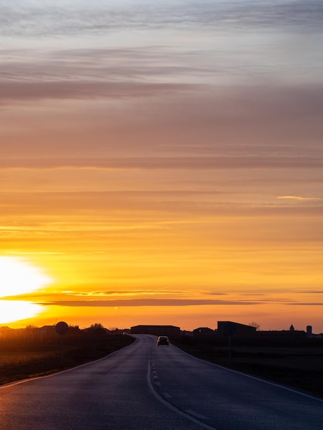 Atardecer en una carretera pavimentada con un automóvil conduciendo y la silueta de una ciudad en el espacio de copia de fondo