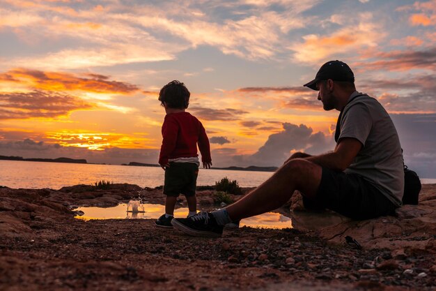 Atardecer en Ibiza de vacaciones joven padre con su hijo disfrutando del mar en San Antonio Abad