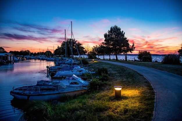 Foto atardecer junto al puerto lleno de barcos con un camino en primer plano.