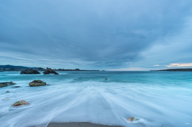 Atardecer nublado en la playa de Arnao con olas moderadas