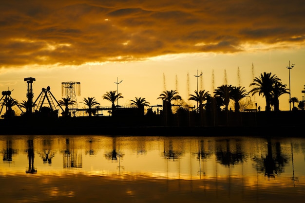 Atardecer en el terraplén de la ciudad turística. Una hilera de siluetas de palmeras contra el fondo del cielo ardiente