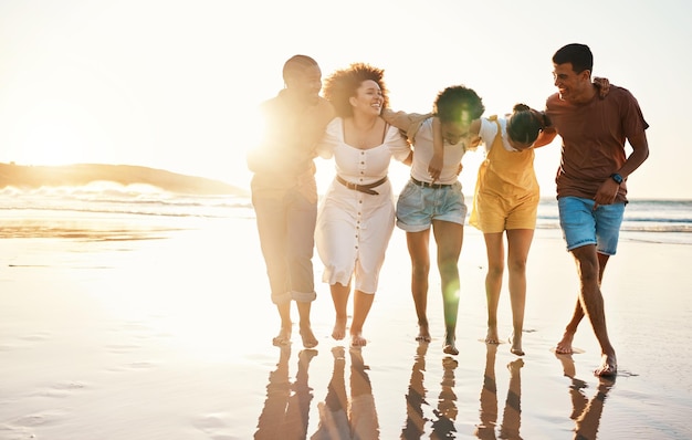 Atardecer de verano y viajar con amigos en la playa para disfrutar de la libertad, el apoyo y la diversidad. Energía de bienestar y felicidad con un grupo de personas caminando junto al mar para disfrutar de una aventura divertida y una maqueta de vacaciones.