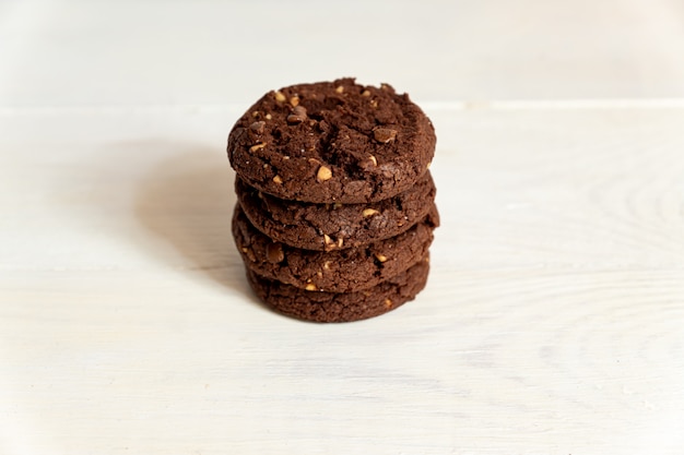 Atascado de galletas caseras de chocolate americano con nueces sobre fondo blanco de madera. Pastelería fresca.