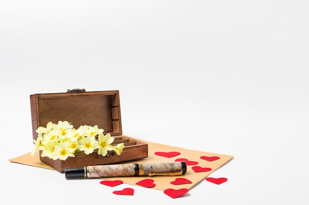 Ataúd vintage de madera, sobre, bolígrafo, corazones rojos de cartón y flores blancas de primavera sobre un fondo blanco.