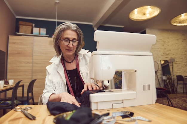 Atelier de design de roupas e alfaiataria Fabricante de costureira caucasiana madura alfaiate costurando roupas em uma máquina de costura de fabricação