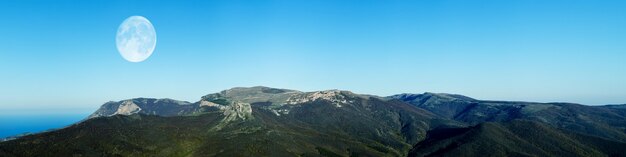 Atemberaubendes Berglandschaftspanorama vor blauem Himmel und Vollmond am Abend