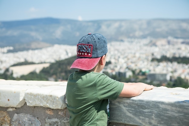 Atenas Grecia Todler kid boy ver restos antiguos vista panorámica desde la colina de Lycabettus paisaje urbano azul mar y cielo de fondo