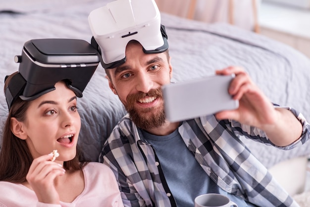 Atención por favor. Feliz pareja emocional positiva en gafas de realidad virtual degustación de palomitas de maíz mientras toma selfie y hombre sonriendo