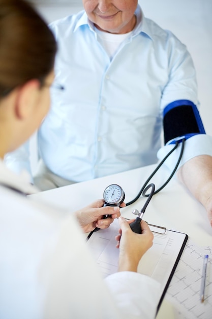 Foto atención médica, ancianos y concepto médico: cierre de una doctora o enfermera que mide la presión arterial a un paciente masculino mayor con tonómetro en el hospital