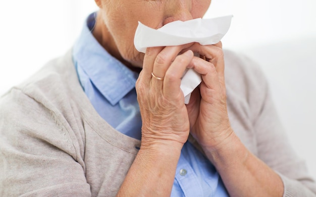 atención de la salud, gripe, higiene, edad y concepto de personas - cierre de una anciana enferma que sopla la nariz a una servilleta de papel en casa