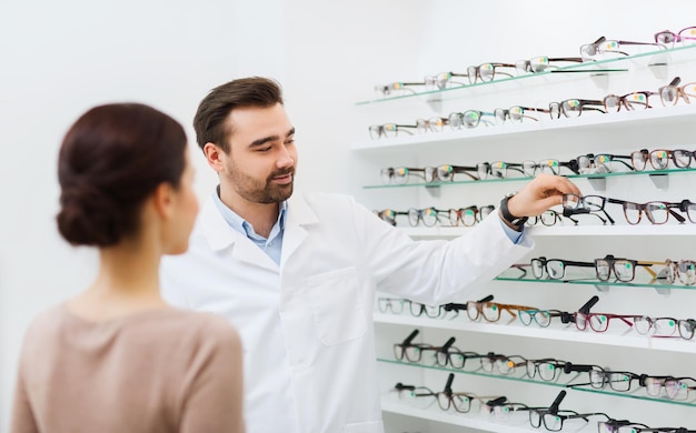 atención de la salud, personas, vista y concepto de visión - óptico que muestra anteojos a la mujer en la tienda de óptica