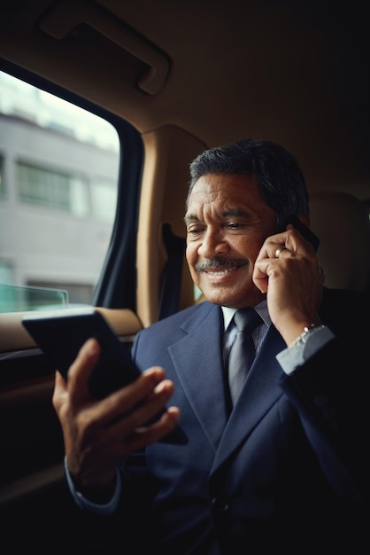 Atender asuntos de negocios en movimiento Foto de un hombre de negocios maduro usando un teléfono y digital mientras viaja en un automóvil