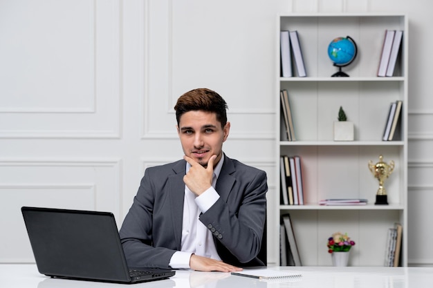 Atendimento ao cliente bonitão inteligente com laptop em blazer de escritório cinza parecendo sério