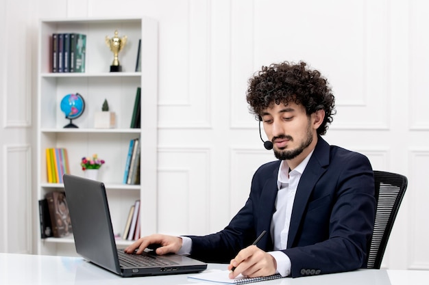 Atendimento ao cliente bonito homem encaracolado em terno de escritório com computador e fone de ouvido trabalhando