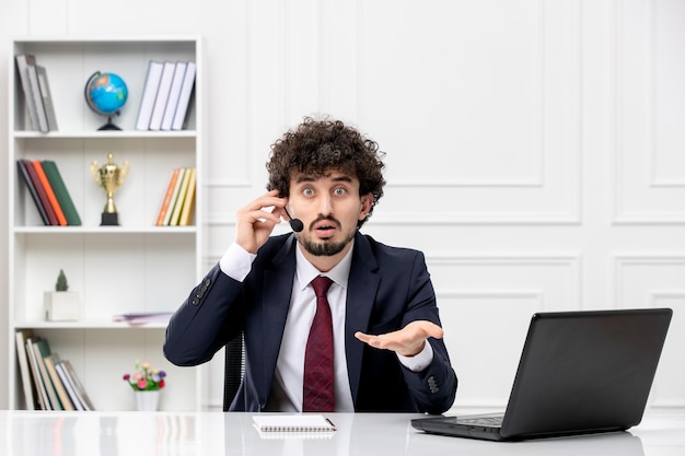 Atendimento ao cliente jovem bonito em terno de escritório com laptop e fone de ouvido confuso na chamada