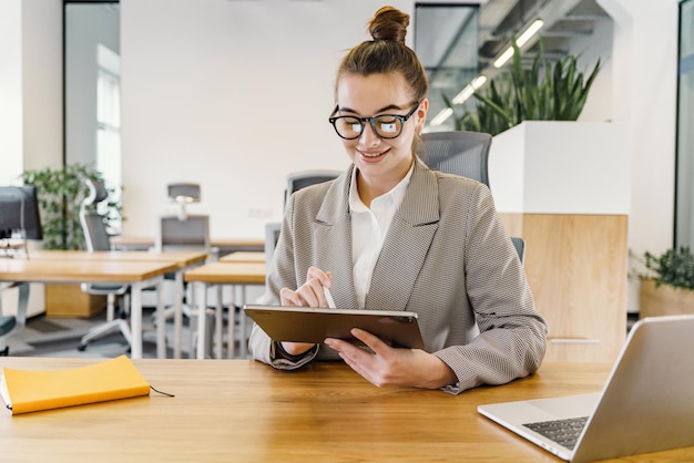 Una atenta mujer de negocios con una chaqueta de perro usa una tableta digital con una computadora portátil en su escritorio