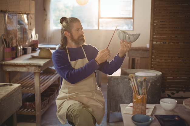 Foto atento hombre alfarero pintando en un tazón