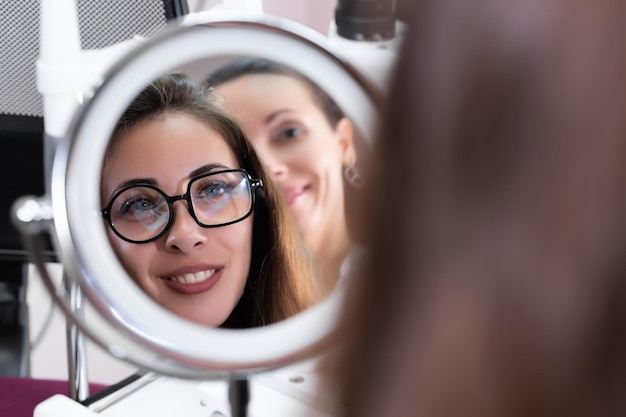 Un atento optometrista ayudó a una bella paciente con la elección de las gafas Recepción en una moderna tienda de gafas de una clínica oftalmológica El paciente se mira en el espejo con el médico